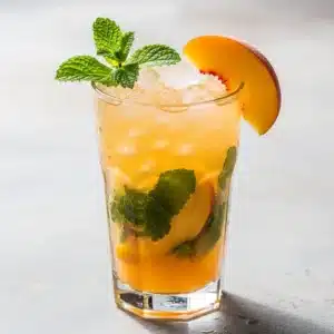 A refreshing peach mojito in a tall glass, garnished with a fresh peach slice and mint sprig.