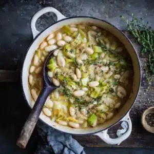 An overhead view of a white Dutch oven filled with creamy butter beans and leeks, showcasing the simple ingredients and rich texture of the vegetarian dish.
