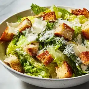 A close-up shot of homemade Caesar dressing being drizzled over crisp romaine lettuce leaves in a wooden bowl.