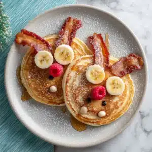 Two cute reindeer pancakes on a light grey plate, showcasing the fluffy pancake texture and charming decorations. A perfect holiday pancake idea.