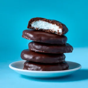A close-up shot of several homemade peppermint patties on parchment paper, showing their glossy chocolate coating before they are fully set.