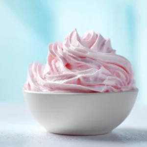 A macro shot showing the light and airy texture of the fluffy strawberry frosting in a white bowl, highlighting its smooth consistency.