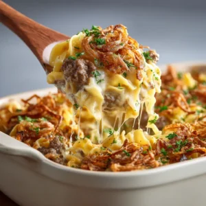 A close-up spoonful of French Onion Beef Casserole, showing the rich beef mixture, tender noodles, and strings of melted cheese.