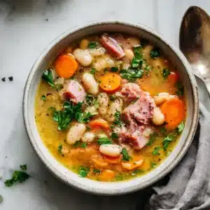 An overhead close-up shot of a hearty slow cooker ham and bean soup in a rustic bowl, garnished with fresh parsley.