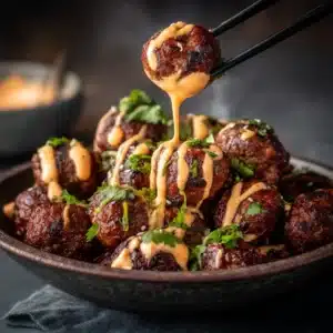 A close-up shot of several Korean BBQ meatballs coated in a glossy, spicy gochujang glaze and sprinkled with sesame seeds.
