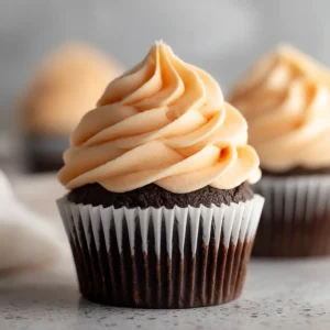A close-up shot of fluffy vanilla pudding buttercream frosting being swirled onto a vanilla cupcake with a piping tip.