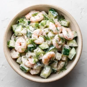 A close-up overhead shot of a creamy cucumber shrimp salad in a white bowl, showing the texture of the shrimp, cucumbers, and dill dressing.