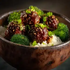 A rustic ceramic bowl filled with homemade Mongolian meatballs, smothered in a sweet and savory sauce and ready to be served.
