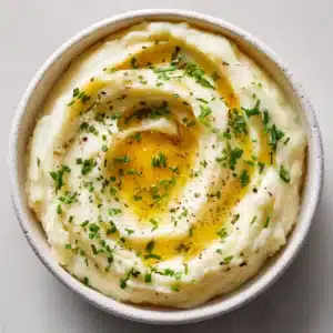 Fresh ingredients for creamy mashed potatoes including Yukon Gold potatoes, melted butter, chives, and cream.