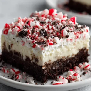 Overhead view of ingredients for No-Bake Candy Cane Dessert, including dark chocolate cookies, cream cheese, vanilla pudding mix, and bright red and white peppermint candy canes.