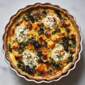 A whole baked winter vegetable quiche in a round fluted white ceramic pan, showing the flaky crust and colorful filling of squash, kale, and ricotta, garnished with thyme.