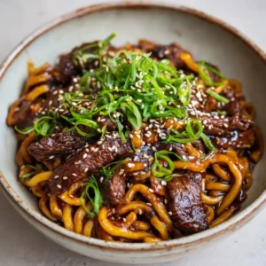 A detailed overhead shot of Sticky Beef Noodles in a bowl. The thick, dark sauce glistens on the chewy noodles and caramelized steak strips. (Sticky Beef Noodles)