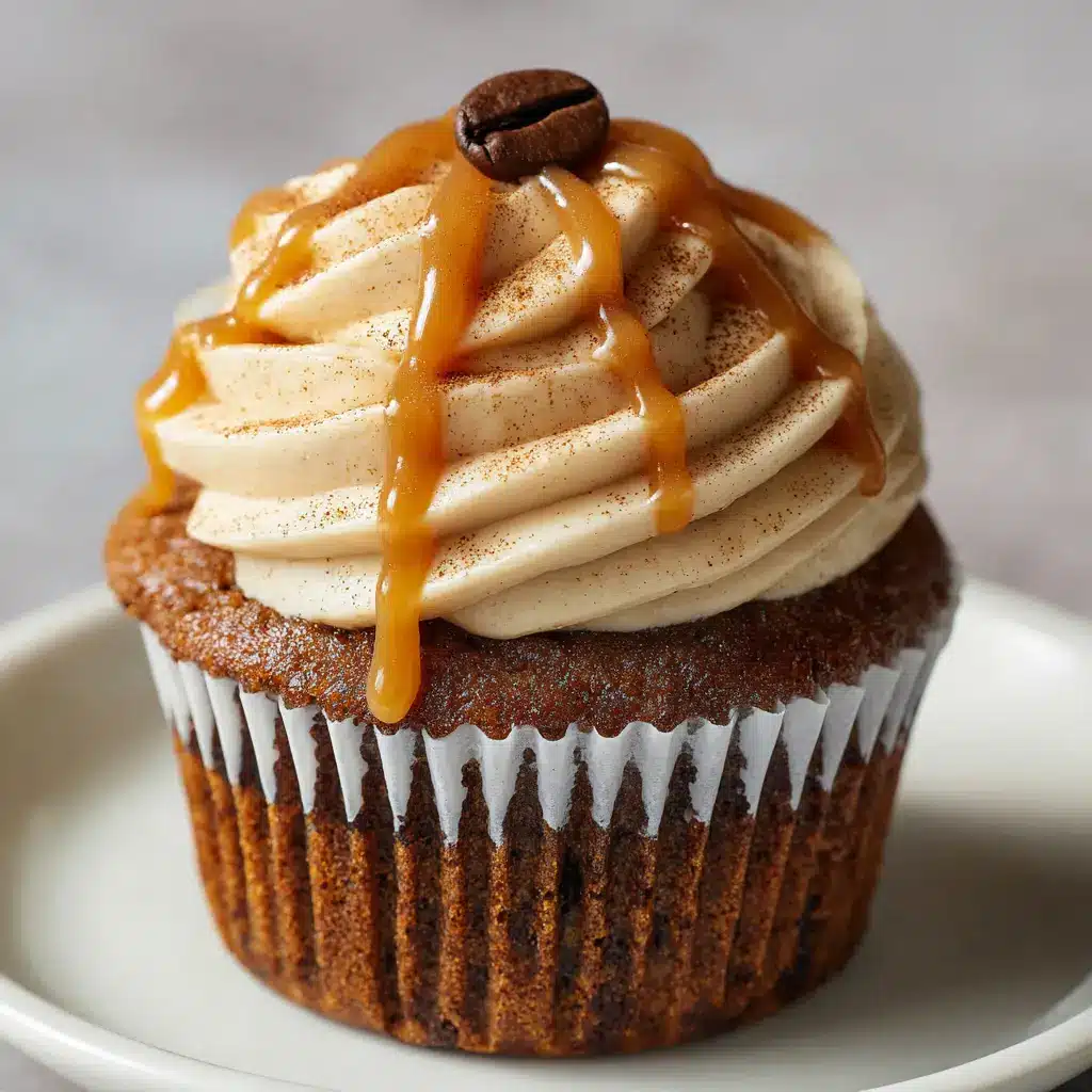 A profile view of a Gingerbread Caramel Latte Cupcake, showing the moist, dark brown spiced sponge and the tall swirl of light beige coffee frosting.