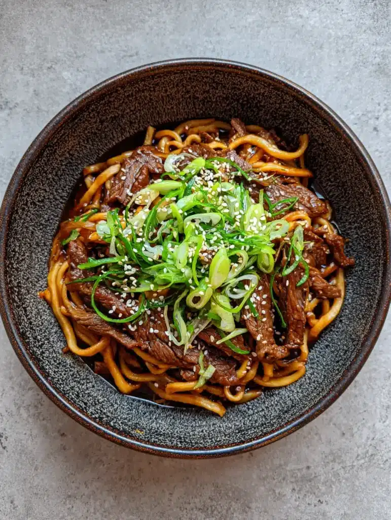 Sticky Beef Noodles featuring thick chewy wheat noodles and seared beef strips in a glossy dark brown sauce.