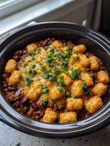 Close up of Slow Cooker Cowboy Casserole showing bubbling orange cheddar cheese with oil droplets and fresh green scallions.