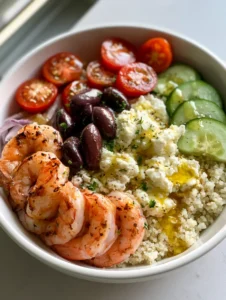 A close-up of a Mediterranean Shrimp Bowl with five large seared shrimp, cucumber crescents, and kalamata olives over white quinoa.