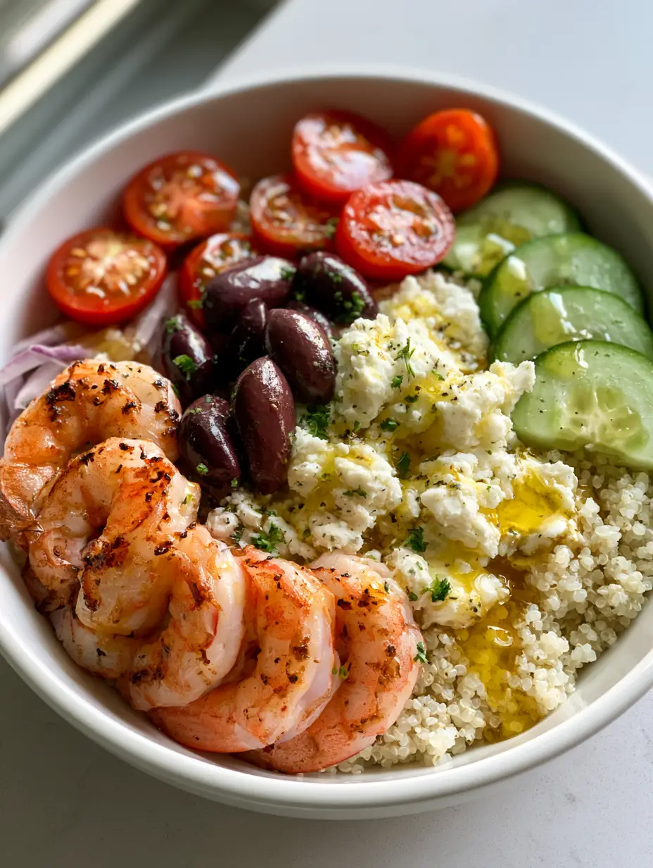 A close-up of a Mediterranean Shrimp Bowl with five large seared shrimp, cucumber crescents, and kalamata olives over white quinoa.