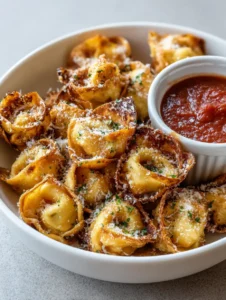 A shallow white bowl filled with crispy golden-brown Air Fryer Cheese Tortellini showing charred edges and parmesan dusting.