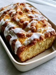 A handheld smartphone photo showing a fresh Southern Peach Bread in a stoneware dish with visible peach chunks and a zigzag glaze.