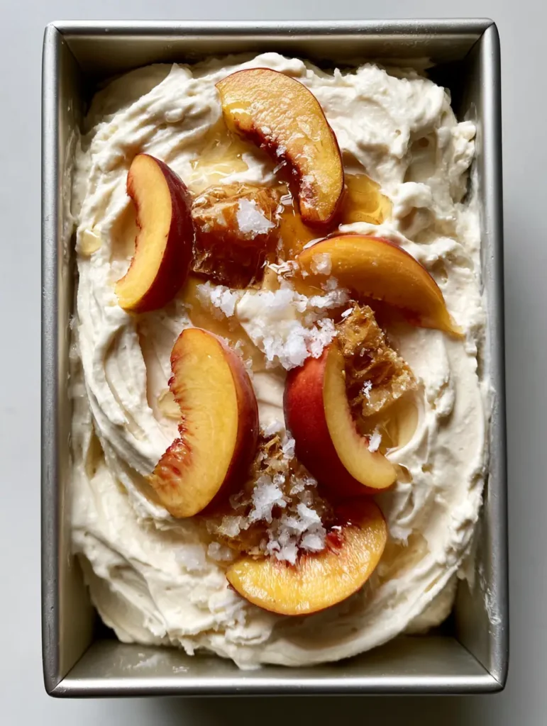 Close-up of No Churn Peach Ice Cream in a metal pan showing flaky sea salt crystals and translucent honey over fresh peaches.