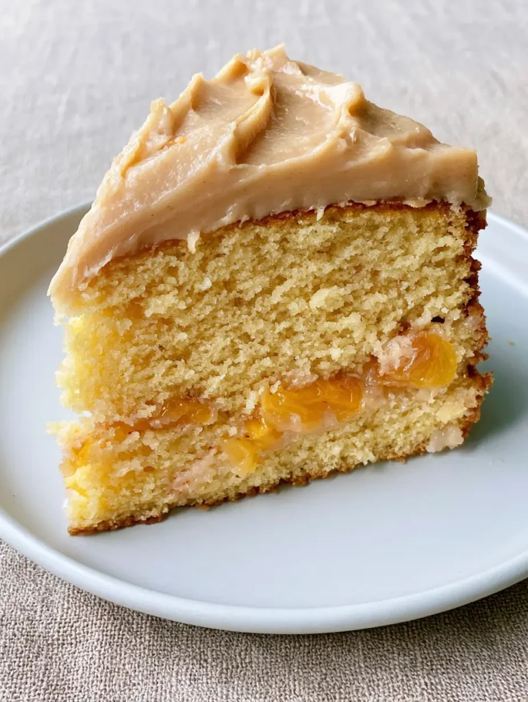 Peach Cake Recipe: A Golden Sponge with Velvet Brown Sugar Frosting 1 A slice of peach cake showing the thick, smooth beige-colored brown sugar frosting with matte-gloss finish. (Peach Cake Recipe)