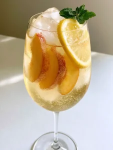 Close up of a Peach White Wine Spritzer showing fine carbonation bubbles and golden peach slices. (Peach White Wine Spritzer)