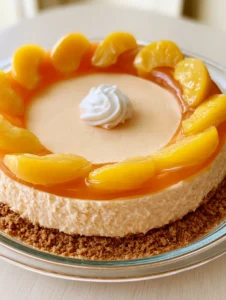 High-angle shot of a No-Bake Peach Cheesecake in a glass dish showing the golden crust and pale-peach filling.