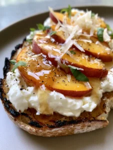 Detailed shot of torn burrata and sliced peaches on a charred baguette slice. (Peach Burrata Crostini)