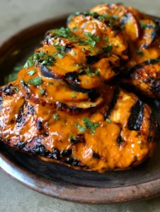 Two grilled chicken breasts with peach chipotle glaze and grilled peach slices on a dark ceramic plate. (Peach Chipotle Grilled Chicken)