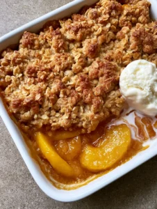 Angled shot showing the thick layers of softened yellow peaches in amber syrup and the textured oatmeal crumble of the Peach Cobbler with Oatmeal Topping.