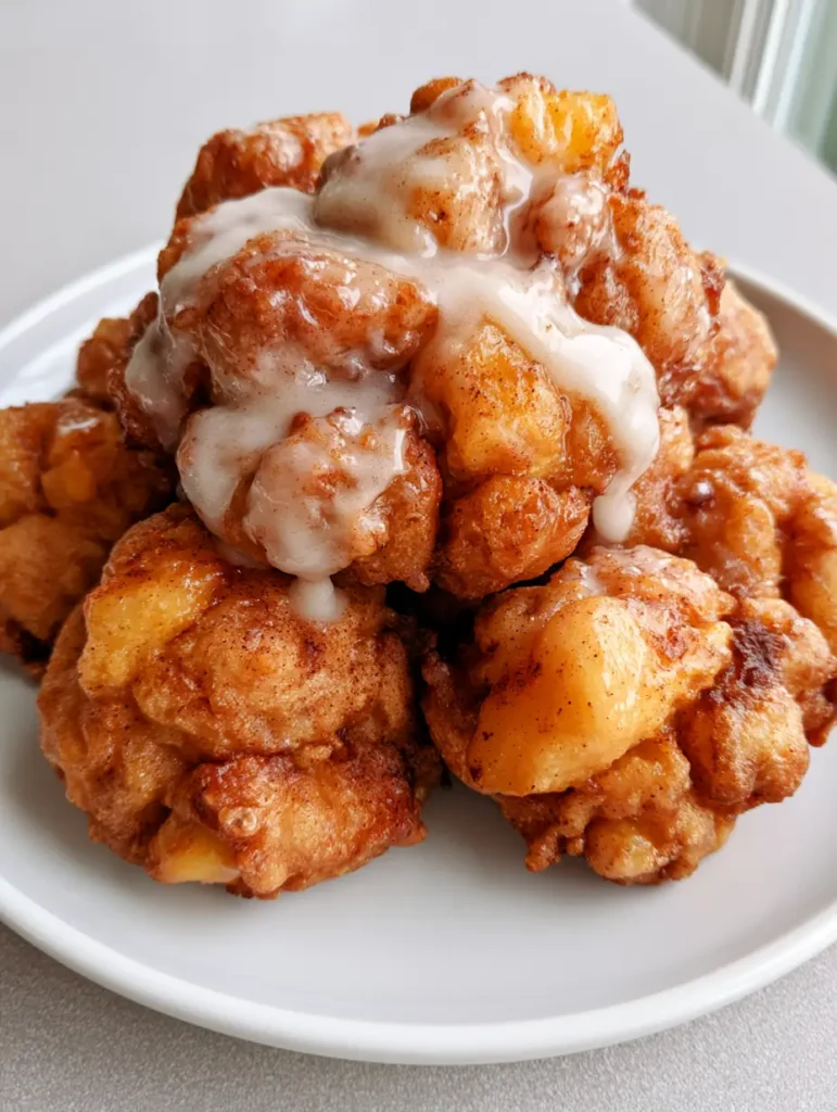 A smartphone style photo of glazed peach fritters on a light grey countertop in natural daylight. (Peach Fritters Recipe)