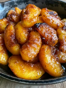 Close-up of Skillet Fried Peaches showing fine flecks of cinnamon and bubbling amber sauce in a dark skillet.
