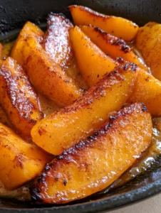 Smartphone photo showing thick peach wedges with vibrant orange flesh and charred caramelized edges. (Pan Fried Peaches)