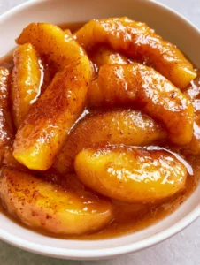 Close-up of tender sliced yellow peaches simmering in a translucent amber syrup. (Stewed Peaches)