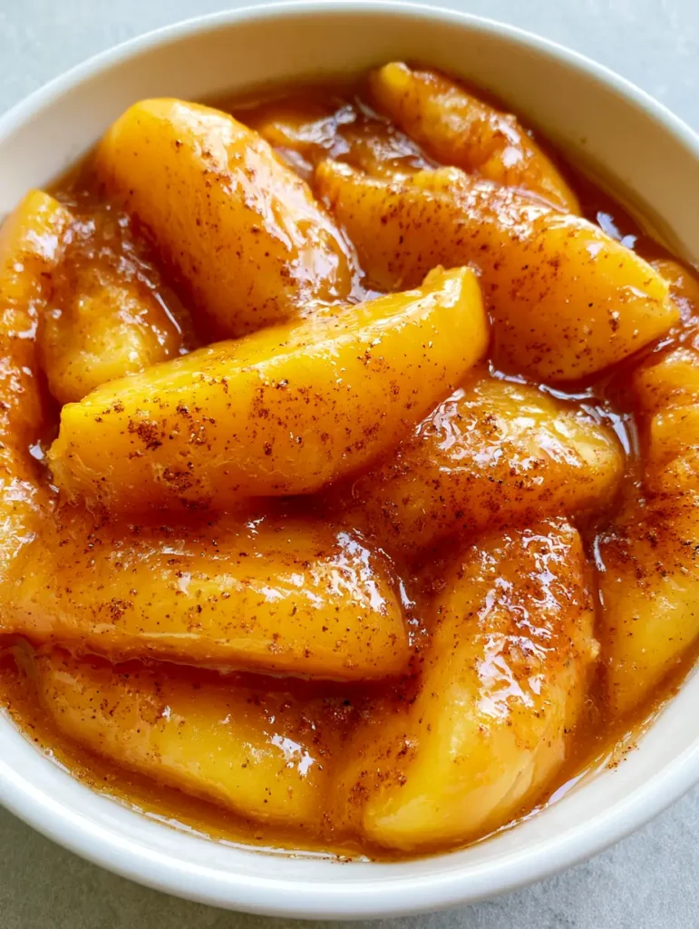 Smartphone photo of stewed peaches in a white bowl on a grey tabletop with natural lighting.