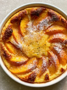 Top-down view of a Peach Clafoutis Recipe showing juicy wedges and vanilla bean specks in a white dish.